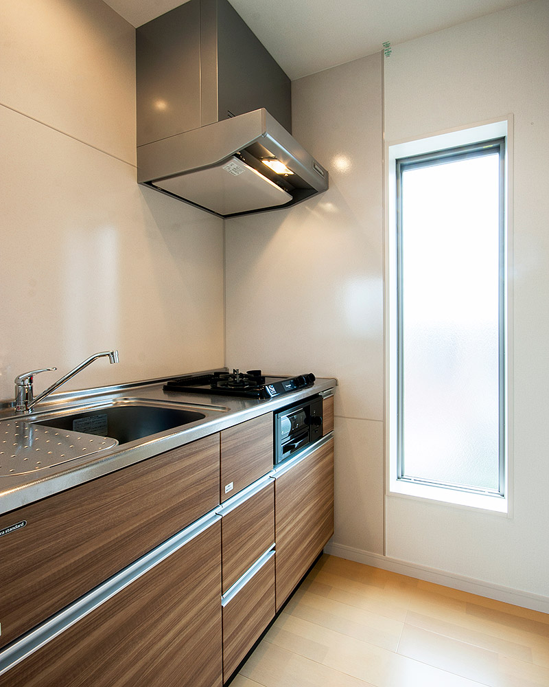 木目調のパネルのキッチン。壁には大きなFIX窓が光を採り込んでいます。